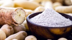Sfondo di tuberi con in risalto un pezzo di manioca e una ciotola contenente farina di manioca. Tutte fonti di amidi