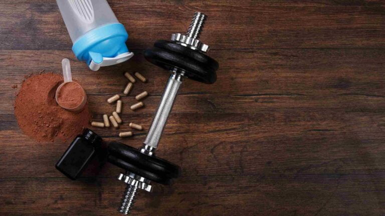 Alcune capsule di aminoacidi ramificati, un manubrio da palestra e una borraccia sopra un pavimento di legno