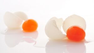 Due uova con il guscio rotto: fuoriescono i tuorli arancioni fonti di vitamina K2