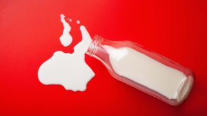 Bottiglia di latte rovesciata su sfondo rosso, concetto visivo di intolleranza al lattosio e allergia alle proteine del latte
