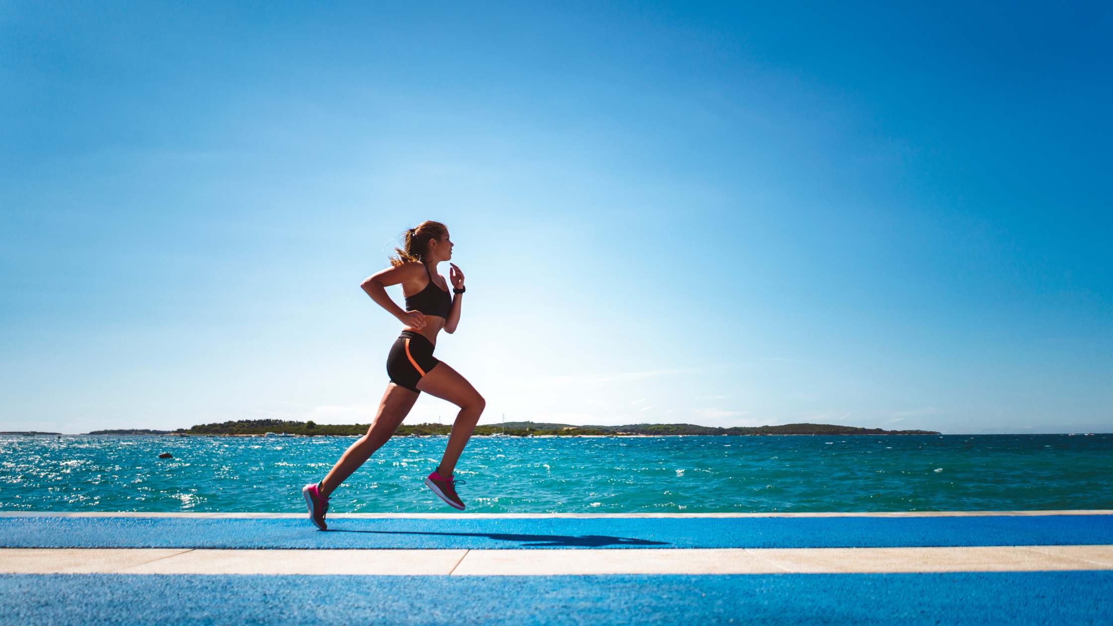 Donna che corre all’aperto vicino al mare, esempio di attività fisica che utilizza i sistemi metabolico energetici