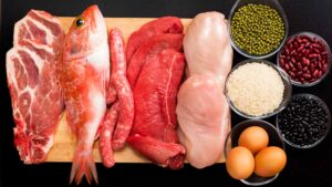 Varie fonti proteiche animali ad alto valore biologico tra cui carne rossa, pollo, pesce e uova, accompagnate da riso e legumi su tagliere di legno.