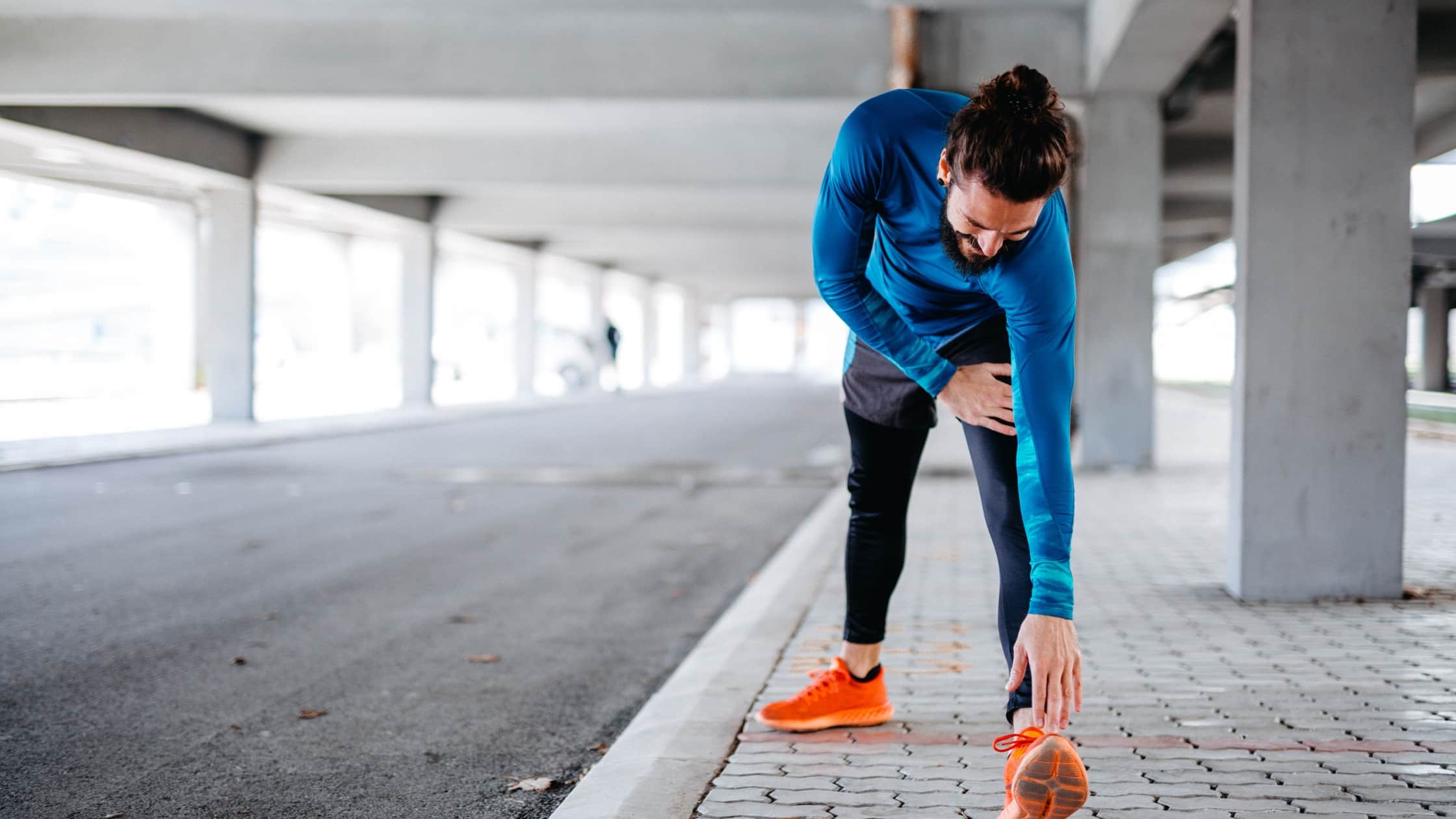un ragazzo a bordo strada allunga le braccia verso i piedi per fare stretching statico
