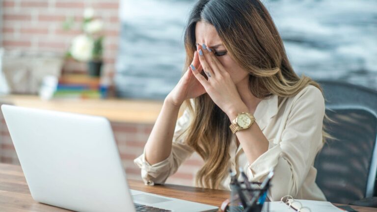 Donna stressata davanti al PC con mano sulla testa, sovraccarico mentale da notifiche, simbolo dello stress moderno