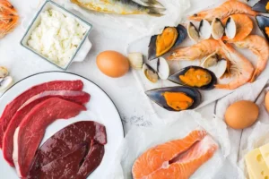 Carne, pesce, crostacei, uova e latticini ricchi di vitamina B12 disposti su un piano chiaro