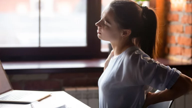 Ragazza alla scrivania che si tocca la schiena dolorante dopo essere stata troppo tempo seduta