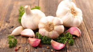 Tre agli interi e tre spicchi d'aglio su una tavola di legno con erbette aromatiche - benefici aglio crudo e allicina