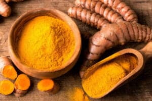 Polvere di curcuma in ciotola e radici fresche tagliate