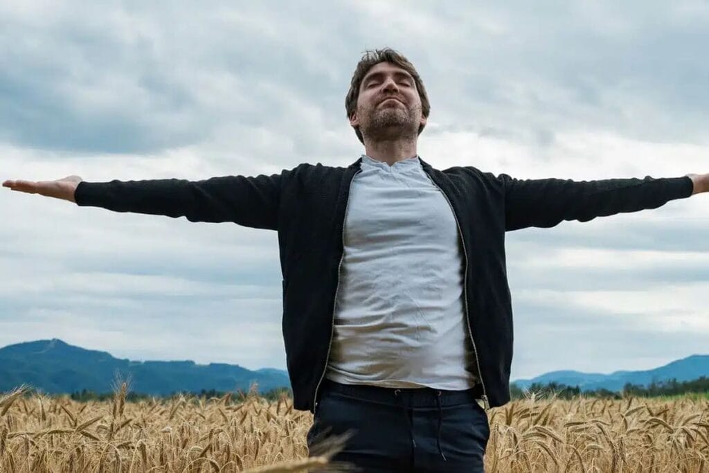 Uomo che pratica mindfulness con le braccia aperte in un campo di grano
