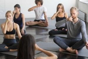 Persone sedute in posizione yoga che praticano la respirazione a narici alternate Nadi Shodhana per favorire calma e concentrazione