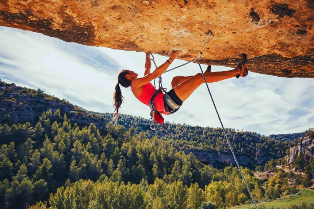 Ragazza si arrampica su una parete di roccia inclinata indietro. Sullo sfondo un suggestivo panorama di montagna in estate