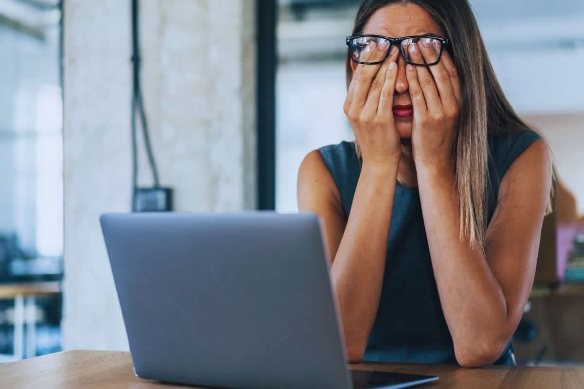 Donna con occhi stanchi e mani sul viso davanti al laptop, simbolo di stress e sistema nervoso affaticato