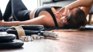 Donna stanca sdraiata a terra dopo un allenamento intenso, simbolo del dolore muscolare post esercizio (DOMS)