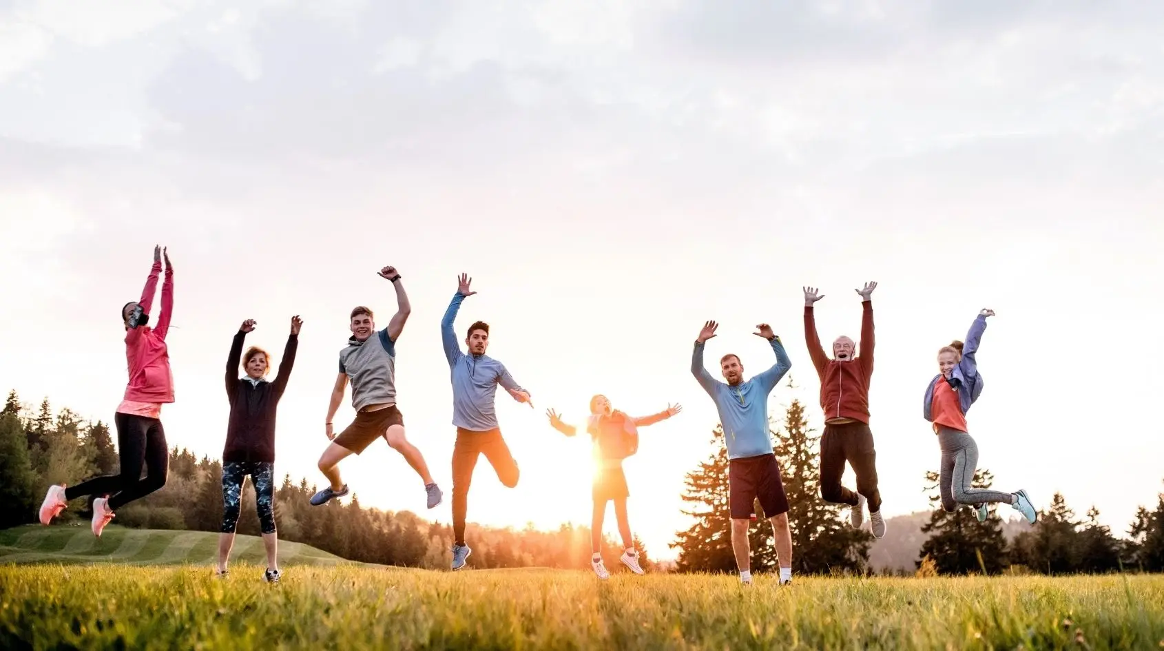 Gruppo eterogeneo di persone di età diversa che salta all’aperto durante un’attività fisica