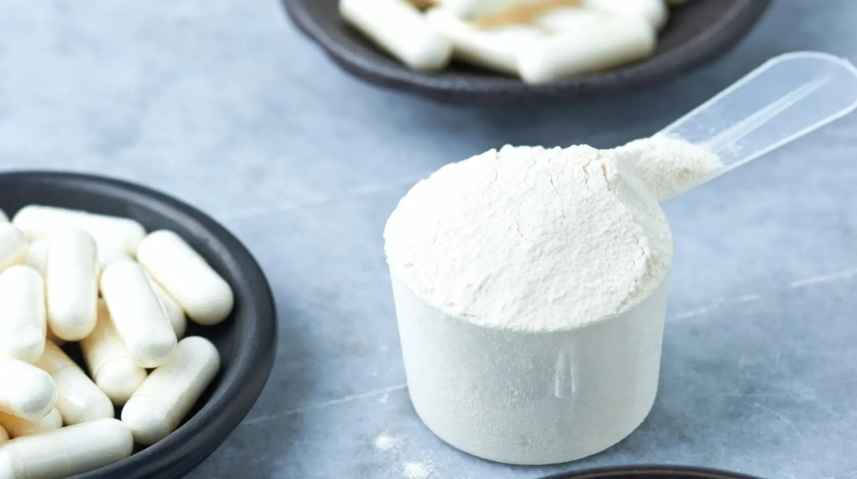 Creatina monoidrato in polvere con misurino e capsule bianche su sfondo neutro