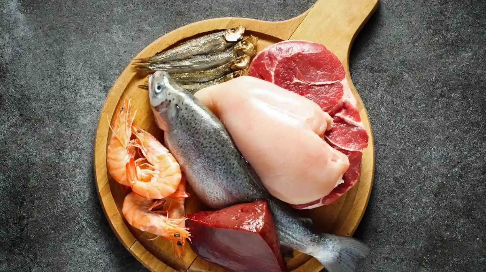 Tagli di carne e pesce freschi disposti su un tagliere per mostrare le principali fonti alimentari naturali di creatina