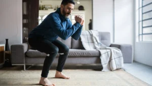 Uomo adulto che esegue uno squat a corpo libero nel soggiorno di casa.