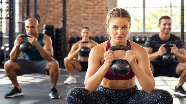 Gruppo di persone esegue squat con kettlebell durante un allenamento di forza in palestra