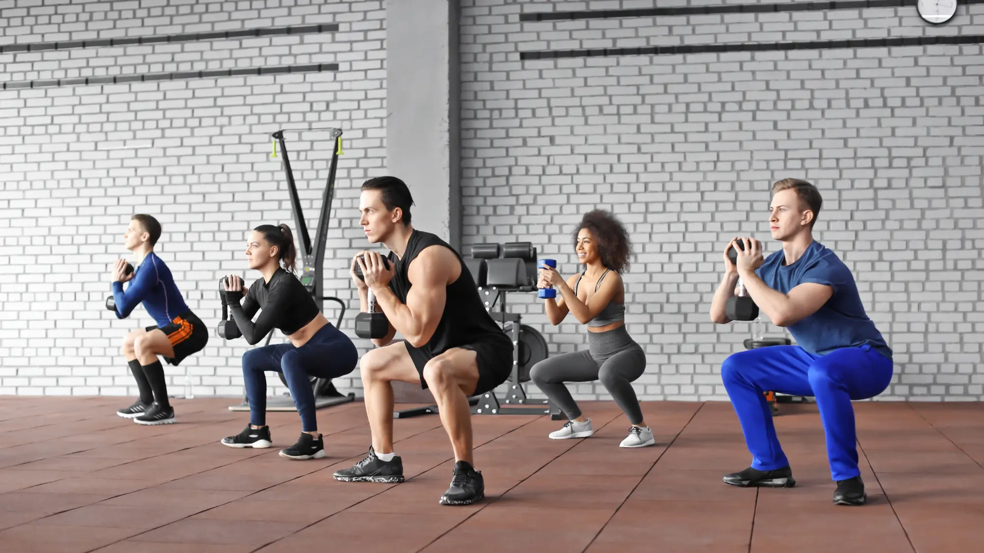 Gruppo di uomini e donne esegue squat con manubri e kettlebell in palestra