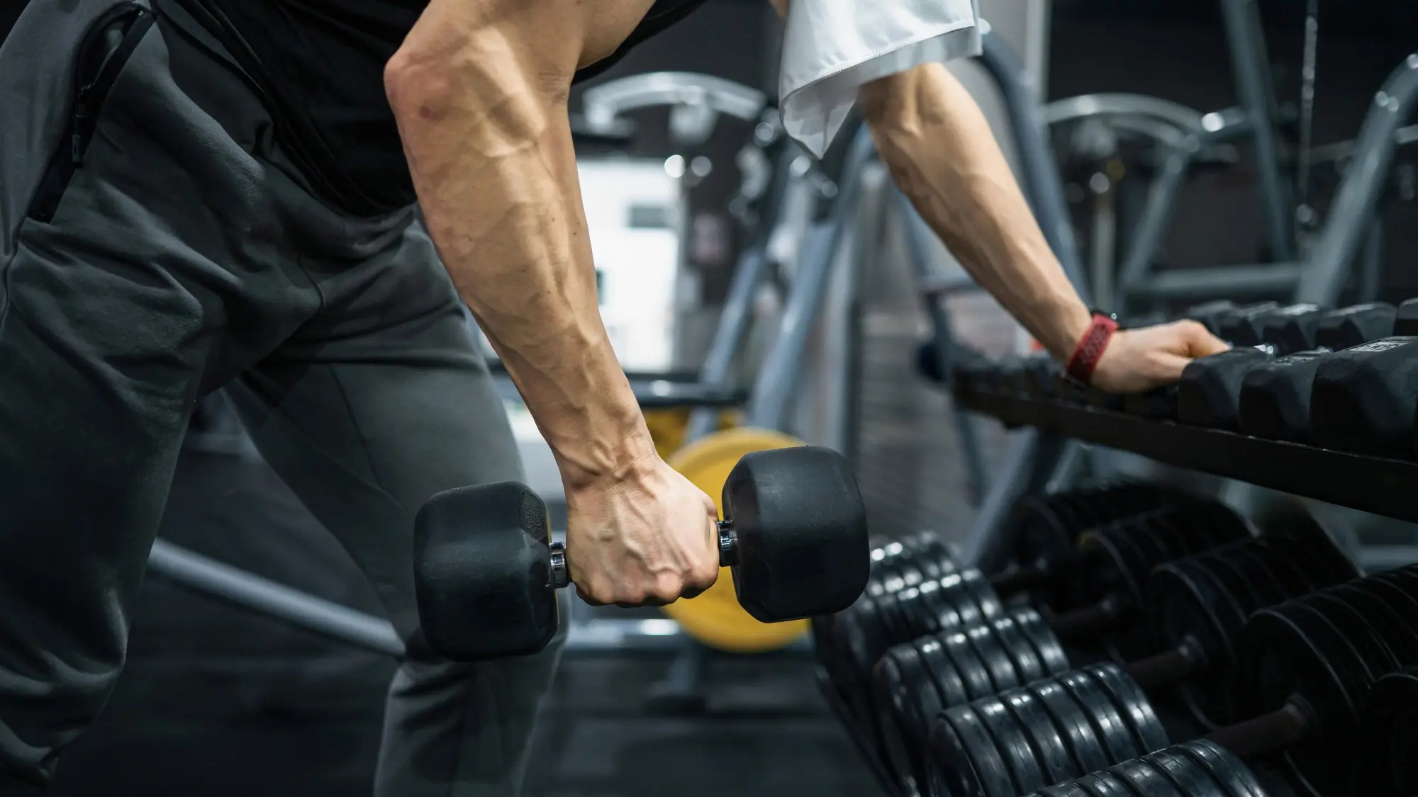 Persona che esegue un rematore con manubrio, appoggiandosi con l'altra mano a un supporto in palestra