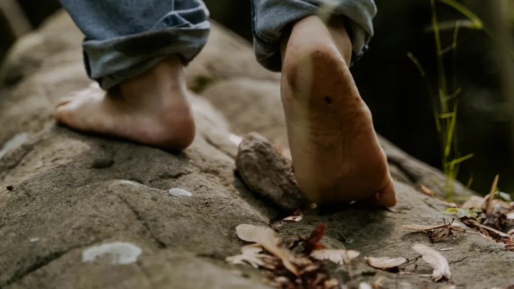 Primo piano di piedi nudi che camminano su un sentiero roccioso, con un piede sollevato durante il passo