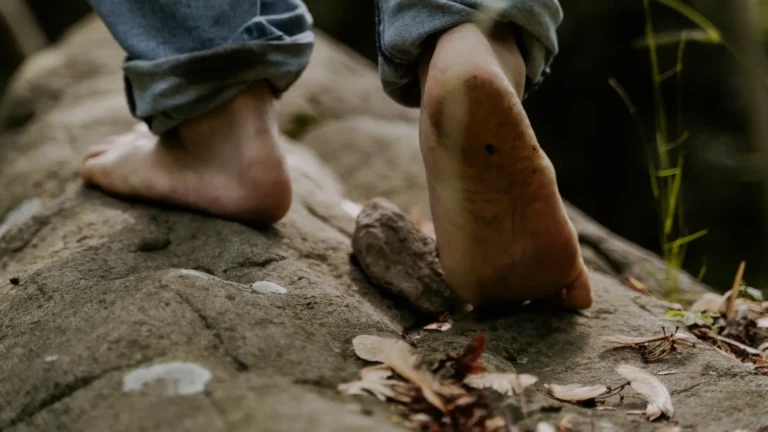 Primo piano di piedi nudi che camminano su un sentiero roccioso, con un piede sollevato durante il passo
