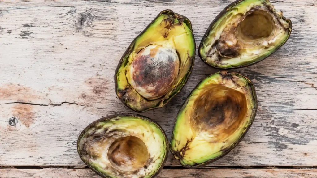 Avocado tagliati a metà con polpa annerita e deteriorata su una superficie di legno