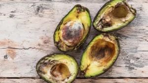 Avocado tagliati a metà con polpa annerita e deteriorata su una superficie di legno