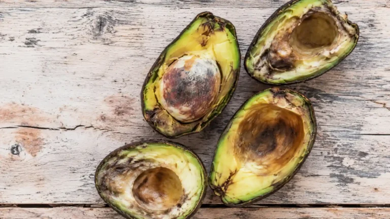 Avocado tagliati a metà con polpa annerita e deteriorata su una superficie di legno