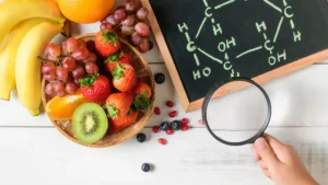 Frutta fresca con banane, fragole, uva e kiwi accanto a una lavagna con una struttura molecolare e una lente d'ingrandimento.