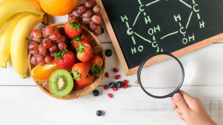 Frutta fresca con banane, fragole, uva e kiwi accanto a una lavagna con una struttura molecolare e una lente d'ingrandimento.