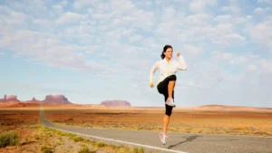 Donna in abbigliamento sportivo esegue un sollevamento dinamico del ginocchio su una strada nel deserto.