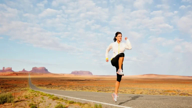 Donna in abbigliamento sportivo esegue un sollevamento dinamico del ginocchio su una strada nel deserto.