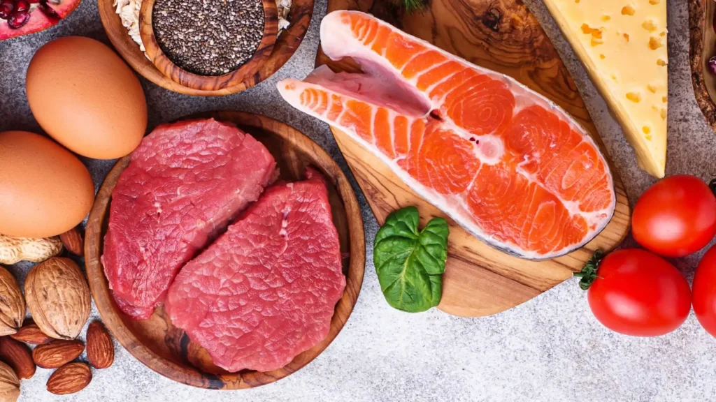 Composizione di alimenti con carne rossa, salmone, uova, formaggio, frutta secca e semi su taglieri di legno.