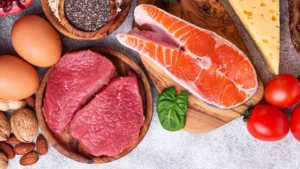 Composizione di alimenti con carne rossa, salmone, uova, formaggio, frutta secca e semi su taglieri di legno.